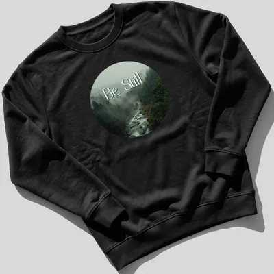 Misty forest scene with 'Be Still' text in earthy tones — printed on a unisex sweatshirt