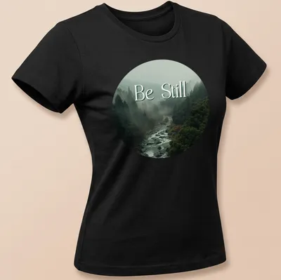 Misty forest scene with 'Be Still' text in earthy tones — printed on a women's shirt