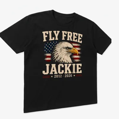 Eagle design with vintage distressed text 'Fly Free Jackie 2012 - 2026' on American flag background — printed on a unisex t-shirt (angled view)