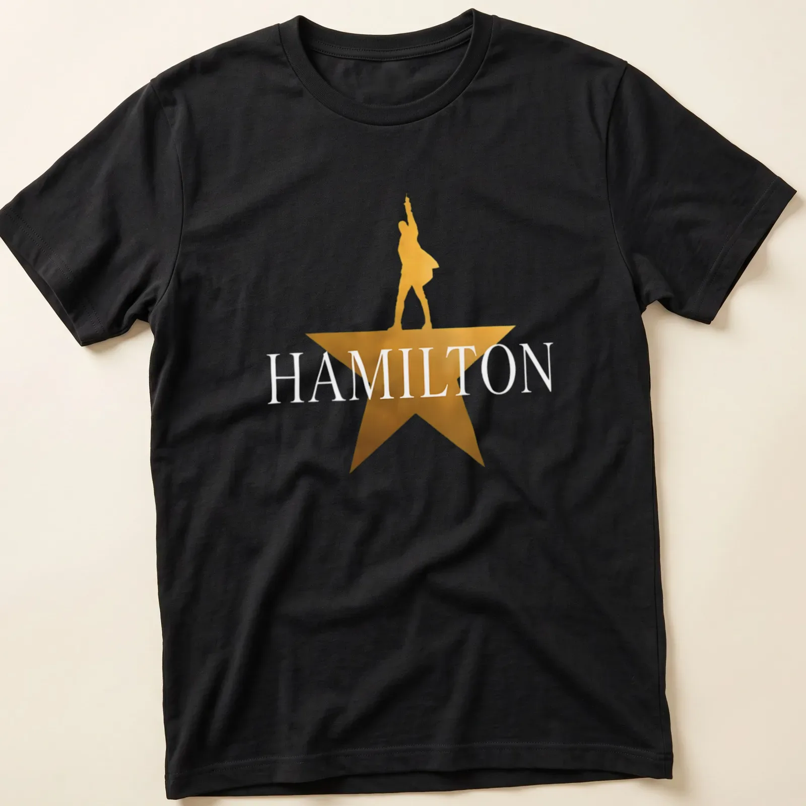 Gold star silhouette of a performer with the word Hamilton above in bold lettering — printed on a unisex t-shirt