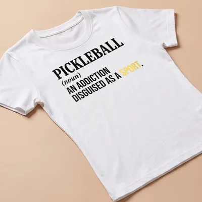 Text-based design featuring the definition of pickleball as an addiction disguised as a sport — printed on a women's shirt