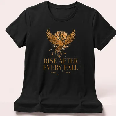 Detailed illustration of a phoenix with the text 'Rise After Every Fall' in gold and orange — printed on a women's shirt