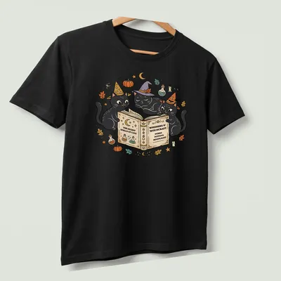 Whimsical design of three black cats wearing witch hats surrounded by text — printed on a unisex t-shirt (angled view)