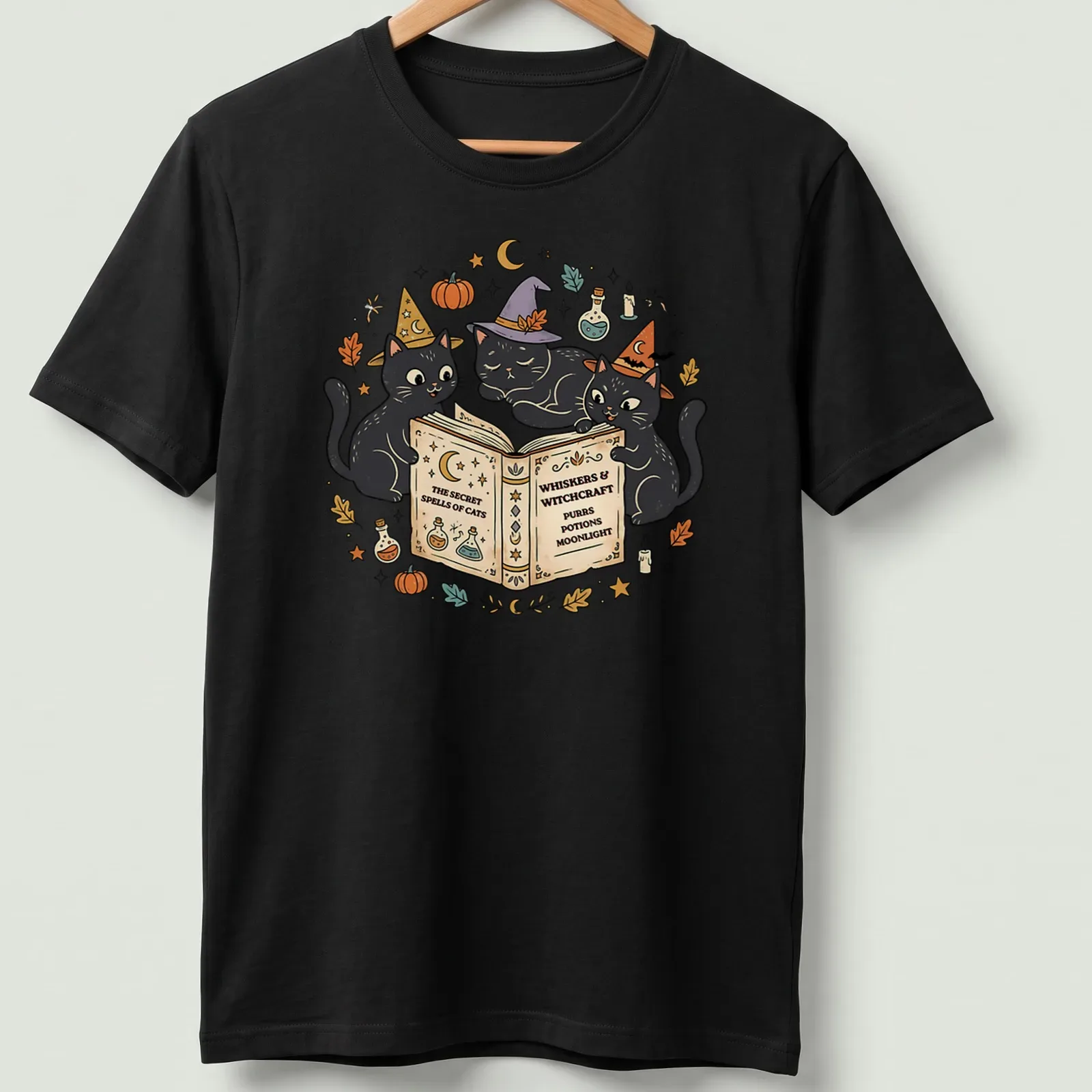 Whimsical design of three black cats wearing witch hats surrounded by text — printed on a unisex t-shirt
