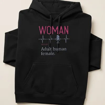 Distressed typography shirt featuring a microphone and heartbeat line with the text 'WOMAN noun Adult human female.' — printed on a unisex hoodie