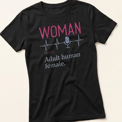 Distressed typography shirt featuring a microphone and heartbeat line with the text 'WOMAN noun Adult human female.' — printed on a women's shirt
